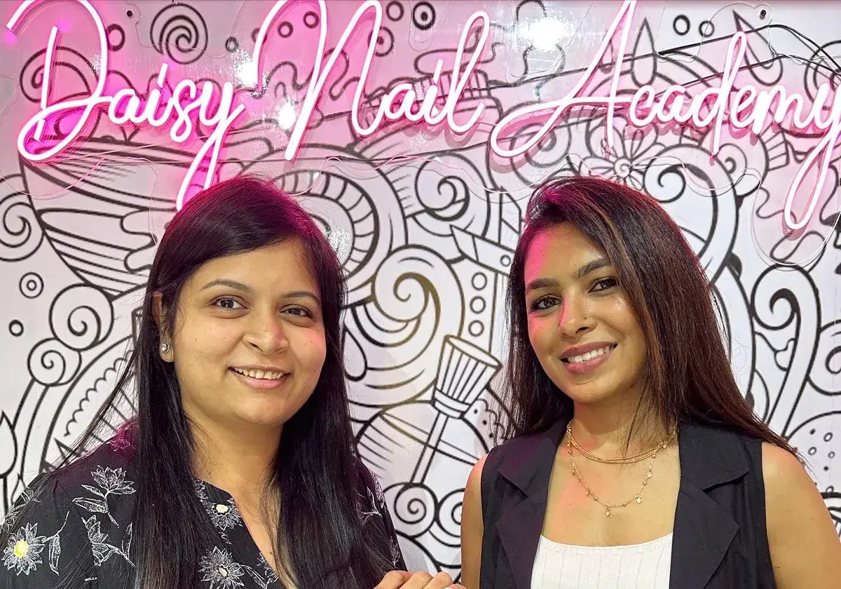 A Daisy Nail Academy trainer and student together beneath the academy neon sign