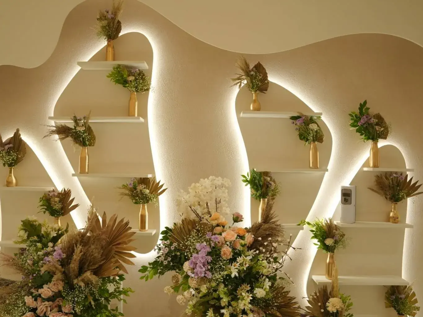 A sculpted, backlit feature wall dressed with dried florals inside a Daisy studio